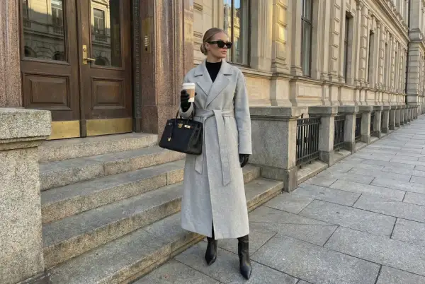 Elegancki szary płaszcz z paskiem, połączony z czarnymi kozakami i torebką, tworzy stylowy look.